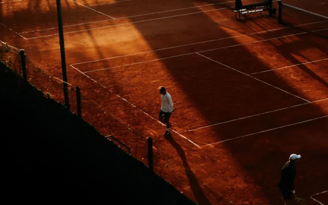 Teren de tenis pe zgură cu jucători, văzut de sus