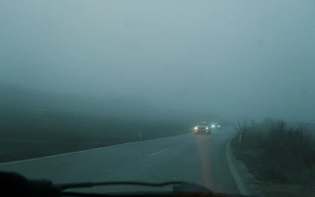 Automobile cu luminile aprinse pe un drum învăluit în ceață