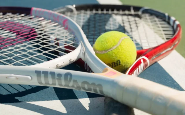 Două rachete de tenis și o minge galbenă pe un teren albastru și verde