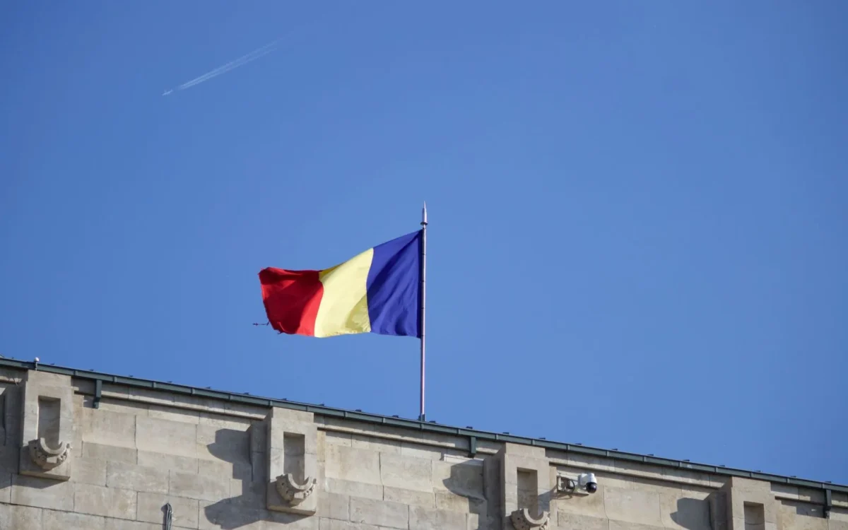 Drapel românesc deasupra unui acoperiș, pe cer albastru