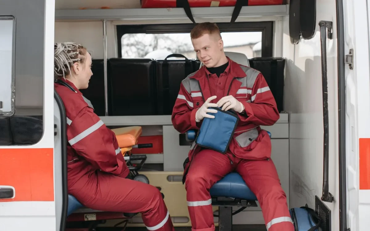 Doi paramedici în uniforme roșii cu o geantă medicală în ambulanță