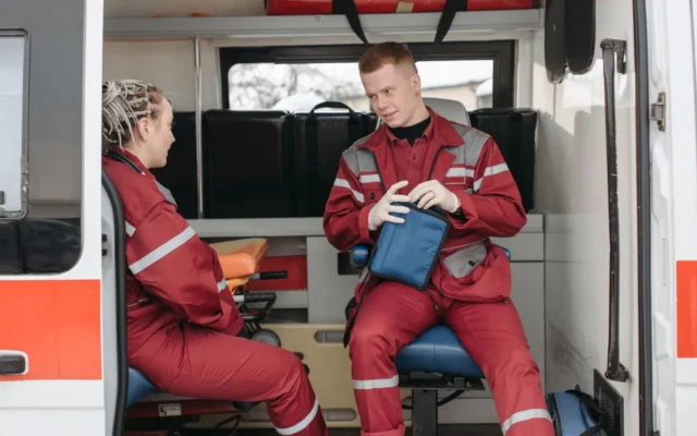 Doi paramedici în uniforme roșii cu o geantă medicală în ambulanță