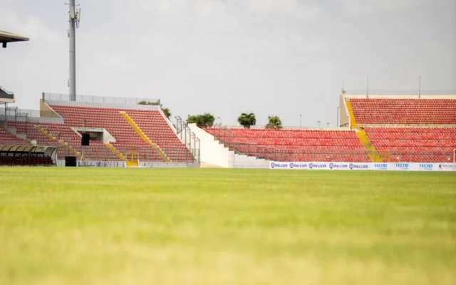 Gazon verde și tribune goale cu scaune roșii pe un stadion de fotbal