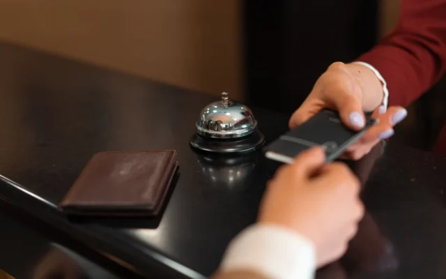 Mâini care înmânează un card la recepția unui hotel, lângă un clopoțel