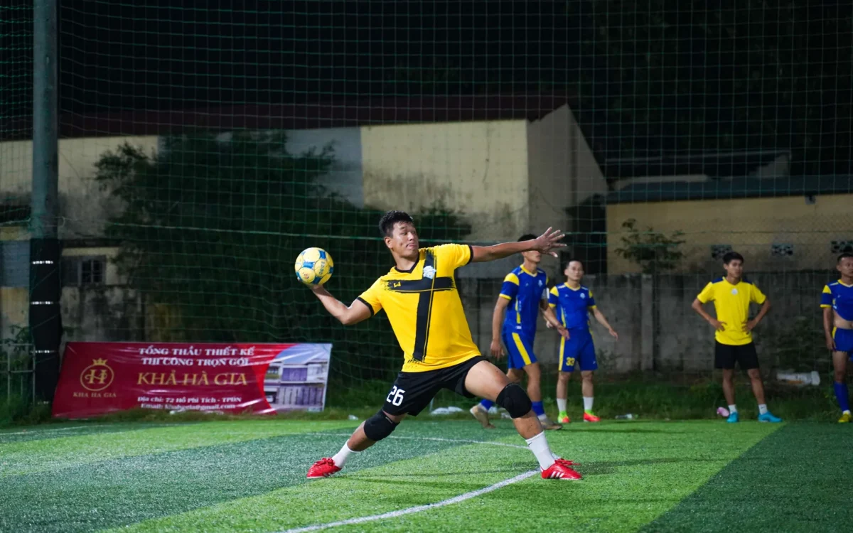 Jucător în galben cu mingea în mână pe un teren de fotbal, noaptea