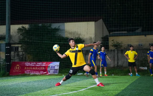 Jucător în galben cu mingea în mână pe un teren de fotbal, noaptea