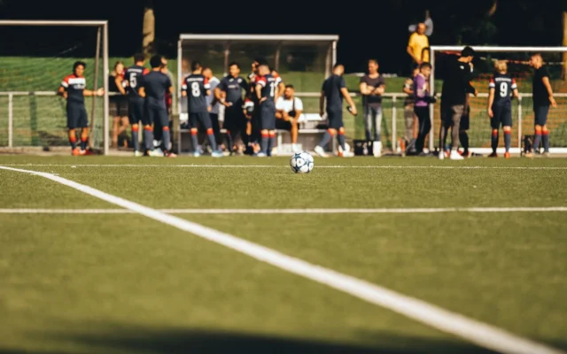 Minge de fotbal pe gazon și jucători în fundal