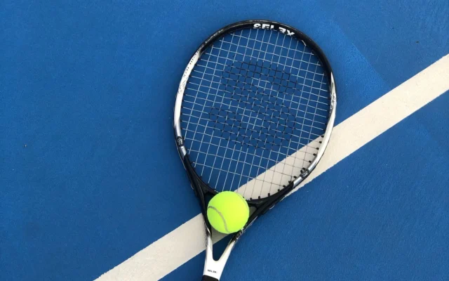 Minge galbenă pe o rachetă de tenis lângă o linie albă pe teren albastru