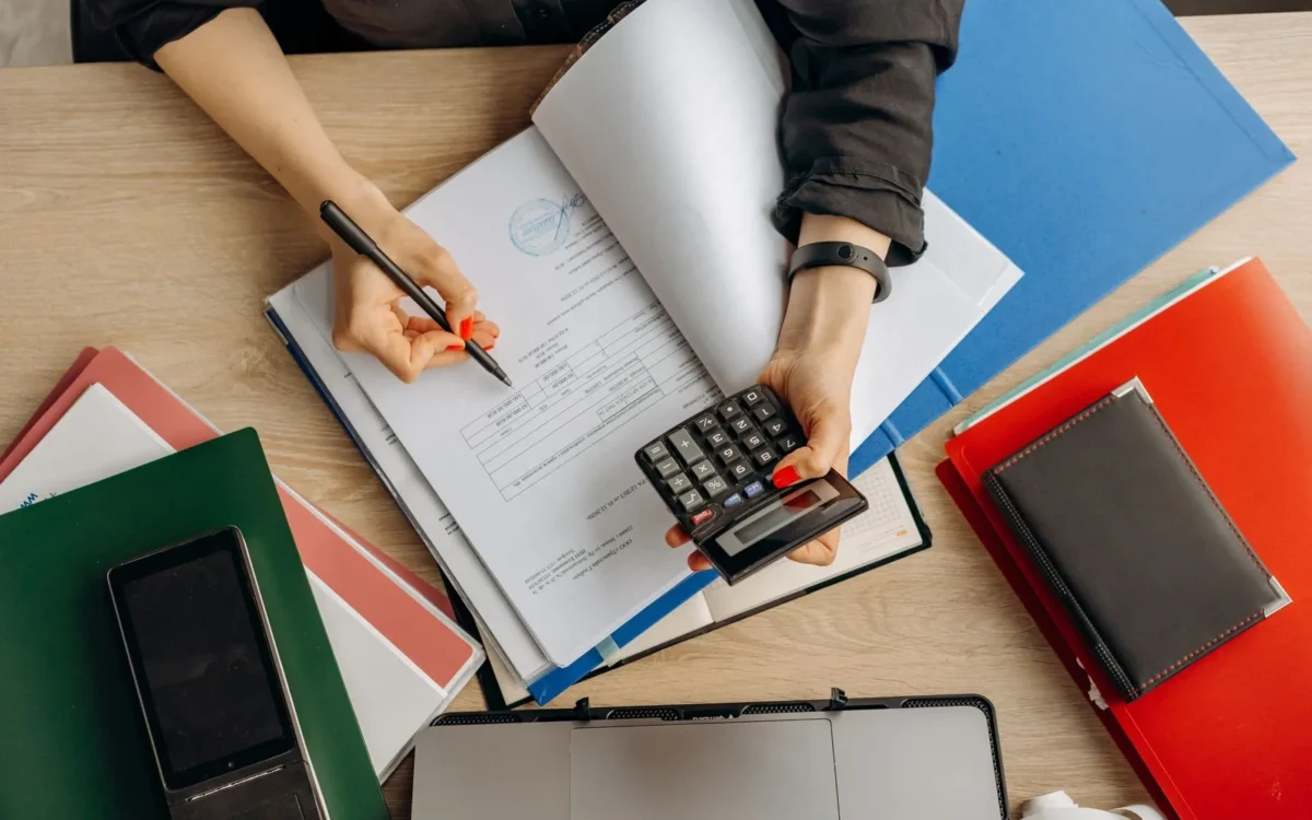 Persoană cu pix și calculator deasupra documentelor de pe birou