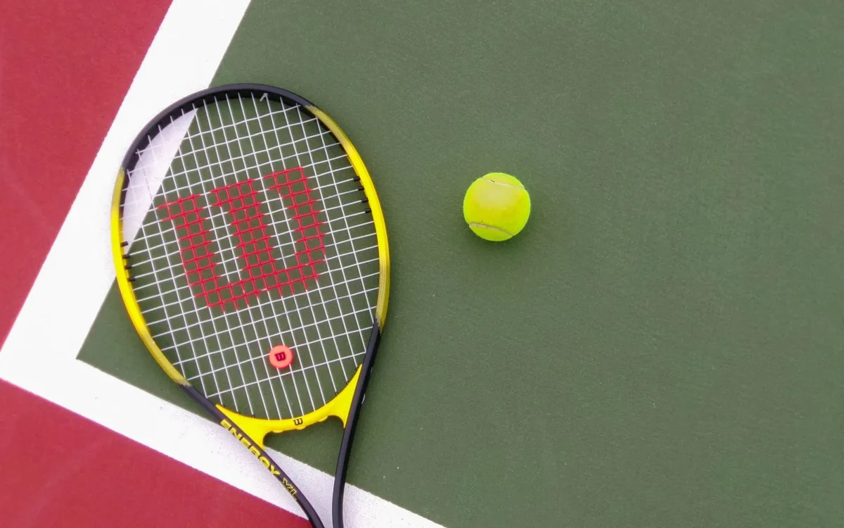 Rachetă galbenă de tenis și minge pe un teren verde și roșu