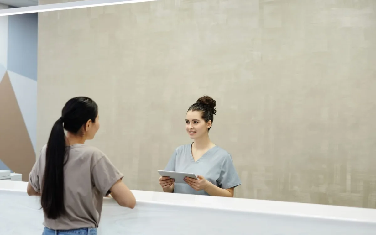 Recepționeră cu tabletă discută cu o persoană într-o clinică