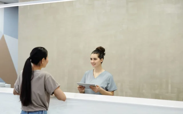 Recepționeră cu tabletă discută cu o persoană într-o clinică